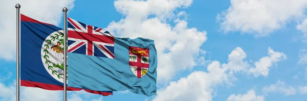Bandera de Belice y Fiyi ondeando en el viento contra el cielo azul nublado blanco juntos. Concepto diplomático, relaciones internacionales . — Foto de Stock