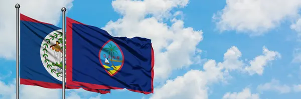 Bandera de Belice y Guam ondeando en el viento contra el cielo azul nublado blanco juntos. Concepto diplomático, relaciones internacionales . — Foto de Stock