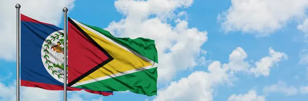 Bandera de Belice y Guyana ondeando en el viento contra el cielo azul nublado blanco juntos. Concepto diplomático, relaciones internacionales . — Foto de Stock