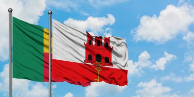 Benin ve Cebelitarık bayrağı birlikte beyaz bulutlu mavi gökyüzüne karşı rüzgarda sallayarak. Diplomasi kavramı, uluslararası ilişkiler.