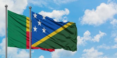 Benin ve Solomon Adaları bayrağı birlikte beyaz bulutlu mavi gökyüzüne karşı rüzgarda sallayarak. Diplomasi kavramı, uluslararası ilişkiler.