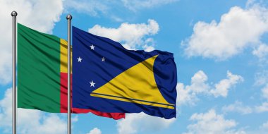 Benin ve Tokelau bayrağı birlikte beyaz bulutlu mavi gökyüzüne karşı rüzgarda sallayarak. Diplomasi kavramı, uluslararası ilişkiler.