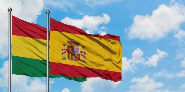 Bolivya ve İspanya bayrağı birlikte beyaz bulutlu mavi gökyüzüne karşı rüzgarda sallayarak. Diplomasi kavramı, uluslararası ilişkiler.