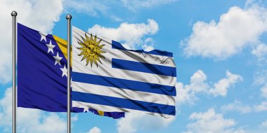 Bosna Hersek ve Uruguay bayrağı birlikte beyaz bulutlu mavi gökyüzüne karşı rüzgarda sallayarak. Diplomasi kavramı, uluslararası ilişkiler.