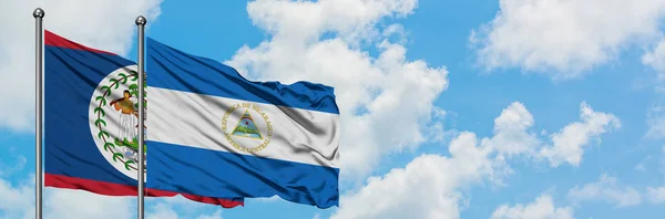 Bandera de Belice y Nicaragua ondeando en el viento contra el cielo azul nublado blanco juntos. Concepto diplomático, relaciones internacionales . — Foto de Stock