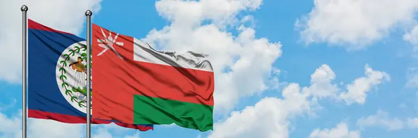 Bandera de Belice y Omán ondeando en el viento contra el cielo azul nublado blanco juntos. Concepto diplomático, relaciones internacionales . — Foto de Stock