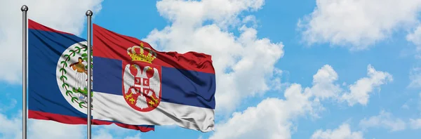 Bandera de Belice y Serbia ondeando en el viento contra el cielo azul nublado blanco juntos. Concepto diplomático, relaciones internacionales . — Foto de Stock