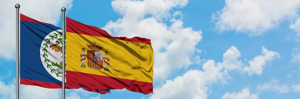 Bandera de Belice y España ondeando en el viento contra el cielo azul nublado blanco juntos. Concepto diplomático, relaciones internacionales . — Foto de Stock