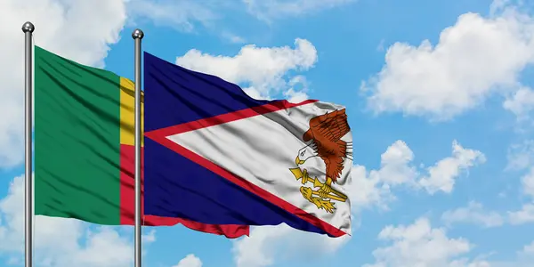 Bandera de Benín y Samoa Americana ondeando en el viento contra el cielo azul nublado blanco juntos. Concepto diplomático, relaciones internacionales . — Foto de Stock