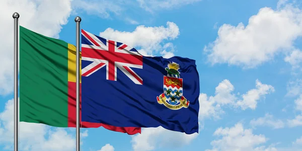 Bandera de Benín y las Islas Caimán ondeando en el viento contra el cielo azul nublado blanco juntos. Concepto diplomático, relaciones internacionales . — Foto de Stock