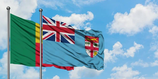 Bandera de Benín y Fiyi ondeando en el viento contra el cielo azul nublado blanco juntos. Concepto diplomático, relaciones internacionales . — Foto de Stock