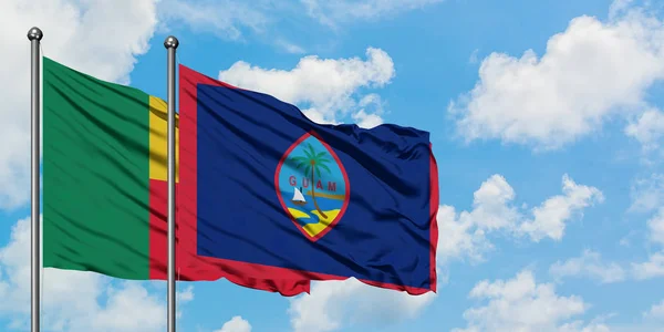 Bandera de Benín y Guam ondeando en el viento contra el cielo azul nublado blanco juntos. Concepto diplomático, relaciones internacionales . — Foto de Stock