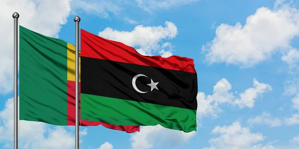 Bandera de Benín y Libia ondeando en el viento contra el cielo azul nublado blanco juntos. Concepto diplomático, relaciones internacionales . — Foto de Stock
