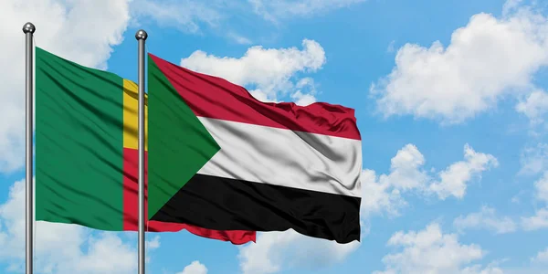 Bandera de Benín y Sudán ondeando en el viento contra el cielo azul nublado blanco juntos. Concepto diplomático, relaciones internacionales . — Foto de Stock