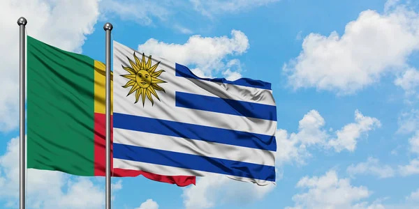 Bandera de Benín y Uruguay ondeando en el viento contra el cielo azul nublado blanco juntos. Concepto diplomático, relaciones internacionales . —  Fotos de Stock