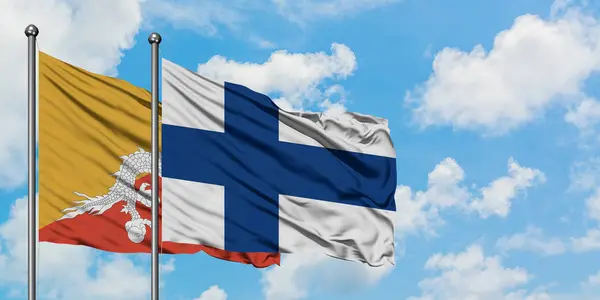 Bhutta a finská vlajka mávajících větrem proti bíle zatažené modré obloze. Diplomacie, mezinárodní vztahy. — Stock fotografie