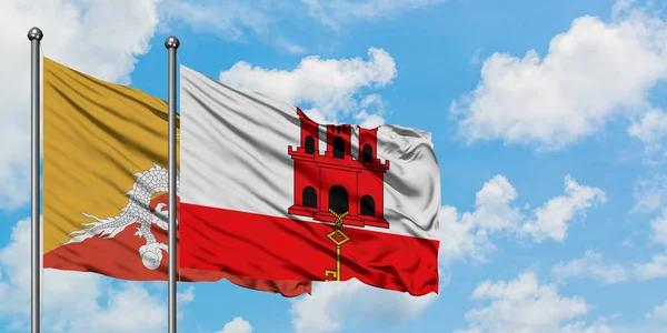 Bhutan and Gibraltar flag waving in the wind against white cloudy blue sky together. Diplomacy concept, international relations. — Stock Photo, Image