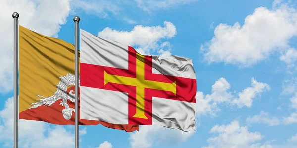 Bandera de Bután y Guernsey ondeando en el viento contra el cielo azul nublado blanco juntos. Concepto diplomático, relaciones internacionales . — Foto de Stock