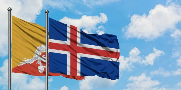 Bandera de Bután e Islandia ondeando en el viento contra el cielo azul nublado blanco juntos. Concepto diplomático, relaciones internacionales . — Foto de Stock