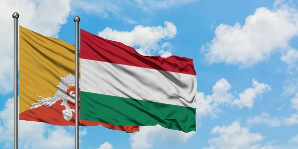 Bandera de Bután y Hungría ondeando en el viento contra el cielo azul nublado blanco juntos. Concepto diplomático, relaciones internacionales . — Foto de Stock