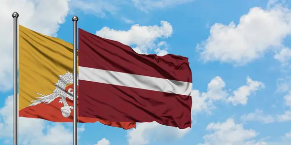 Butão e Letônia acenando com a bandeira no vento contra o céu azul nublado branco juntos. Conceito de diplomacia, relações internacionais . — Fotografia de Stock