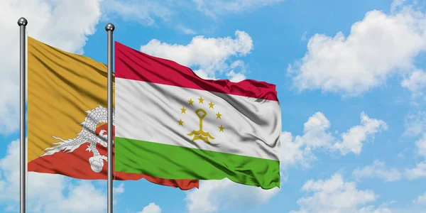 Bandera de Bután y Tayikistán ondeando en el viento contra el cielo azul nublado blanco juntos. Concepto diplomático, relaciones internacionales . — Foto de Stock