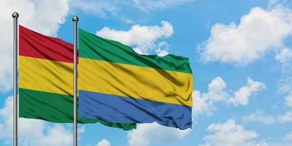 Boliwia i Gabon flaga machając w wiatr przed białym zachmurzone błękitne niebo razem. Koncepcja dyplomacji, stosunki międzynarodowe. — Zdjęcie stockowe