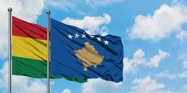 Bandera de Bolivia y Kosovo ondeando en el viento contra el cielo azul nublado blanco juntos. Concepto diplomático, relaciones internacionales . — Foto de Stock