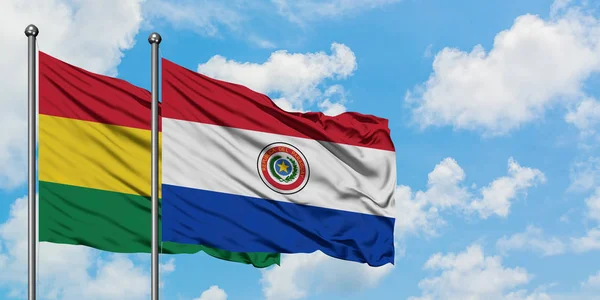Bandera de Bolivia y Paraguay ondeando en el viento contra el cielo azul nublado blanco juntos. Concepto diplomático, relaciones internacionales . — Foto de Stock