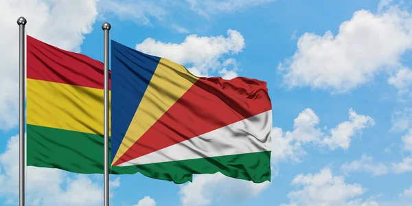 Bolívia e Seychelles bandeira acenando no vento contra branco céu azul nublado juntos. Conceito de diplomacia, relações internacionais . — Fotografia de Stock