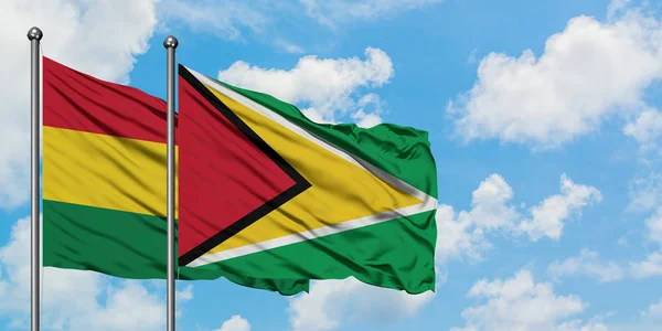 Bandera de Bolivia y Guyana ondeando en el viento contra el cielo azul nublado blanco juntos. Concepto diplomático, relaciones internacionales . — Foto de Stock