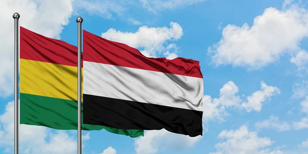 Bandera de Bolivia y Yemen ondeando en el viento contra el cielo azul nublado blanco juntos. Concepto diplomático, relaciones internacionales . — Foto de Stock