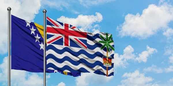 ボスニア・ヘルツェゴビナとイギリス領インド洋地域の旗が一緒に白い曇り青い空に対して風に振る。外交概念、国際関係. — ストック写真