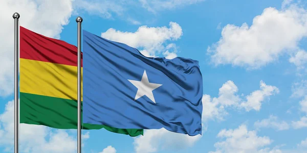 Bandera de Bolivia y Somalia ondeando en el viento contra el cielo azul nublado blanco juntos. Concepto diplomático, relaciones internacionales . — Foto de Stock