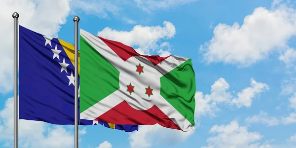 Bandera de Bosnia Herzegovina y Burundi ondeando en el viento contra el cielo azul nublado blanco juntos. Concepto diplomático, relaciones internacionales . — Foto de Stock