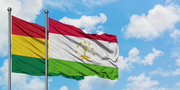 Bandera de Bolivia y Tayikistán ondeando en el viento contra el cielo azul nublado blanco juntos. Concepto diplomático, relaciones internacionales . — Foto de Stock