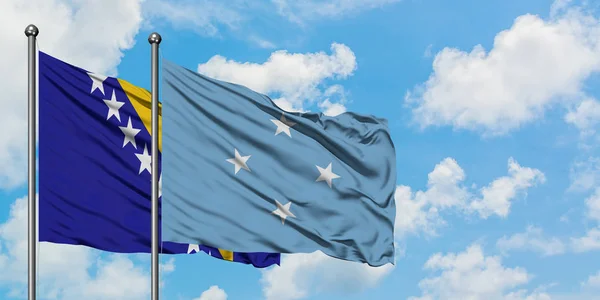 ボスニア・ヘルツェゴビナとミクロネシアの旗が一緒に白い曇り青い空に対して風に手を振る。外交概念、国際関係. — ストック写真