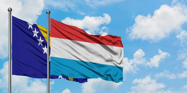 A Bósnia-Herzegovina e a bandeira do Luxemburgo agitando ao vento contra o céu azul nublado branco juntas. Conceito de diplomacia, relações internacionais . — Fotografia de Stock