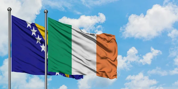 Bandera de Bosnia Herzegovina e Irlanda ondeando en el viento contra el cielo azul nublado blanco juntos. Concepto diplomático, relaciones internacionales . —  Fotos de Stock