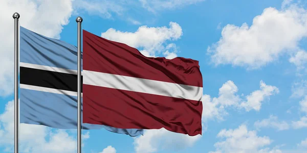 Drapeau du Botswana et de la Lettonie agitant dans le vent contre ciel bleu nuageux blanc ensemble. Concept de diplomatie, relations internationales . — Photo