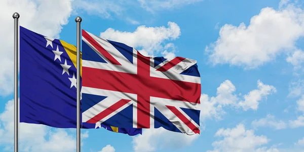 Bandera de Bosnia Herzegovina y el Reino Unido ondeando en el viento contra el cielo azul nublado blanco juntos. Concepto diplomático, relaciones internacionales . — Foto de Stock