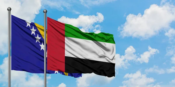 Bosnia Herzegovina y los Emiratos Árabes Unidos ondean en el viento contra el cielo azul nublado blanco juntos. Concepto diplomático, relaciones internacionales . — Foto de Stock