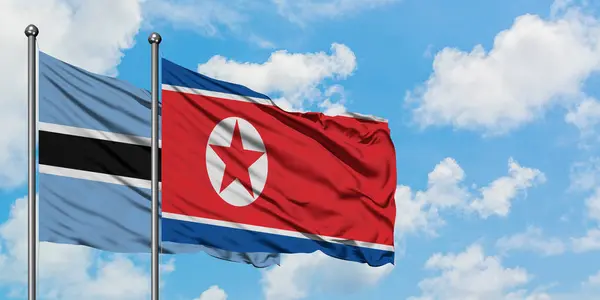 Η σημαία της Μποτσουάνα και της Βόρειας Κορέας κουνώντας τον άνεμο ενάντια στον λευκό θολό γαλάζιο ουρανό μαζί. Φιλοσοφία της διπλωματίας, διεθνείς σχέσεις. — Φωτογραφία Αρχείου