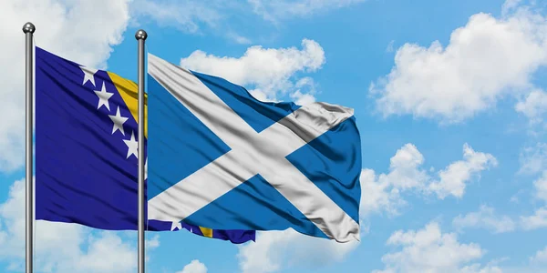 Bósnia-Herzegovina e Escócia bandeira acenando no vento contra o céu azul nublado branco juntos. Conceito de diplomacia, relações internacionais . — Fotografia de Stock