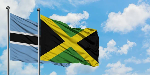 Bandera de Botswana y Jamaica ondeando en el viento contra el cielo azul nublado blanco juntos. Concepto diplomático, relaciones internacionales . — Foto de Stock