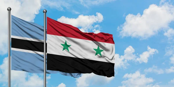 Bandera de Botswana y Siria ondeando en el viento contra el cielo azul nublado blanco juntos. Concepto diplomático, relaciones internacionales . — Foto de Stock