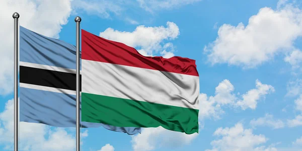 Bandera de Botswana y Hungría ondeando en el viento contra el cielo azul nublado blanco juntos. Concepto diplomático, relaciones internacionales . — Foto de Stock