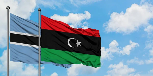Bandera de Botswana y Libia ondeando en el viento contra el cielo azul nublado blanco juntos. Concepto diplomático, relaciones internacionales . — Foto de Stock