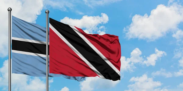 Botswana en Trinidad en Tobago vlag zwaaien in de wind tegen witte bewolkte blauwe hemel samen. Diplomatie concept, internationale betrekkingen. — Stockfoto