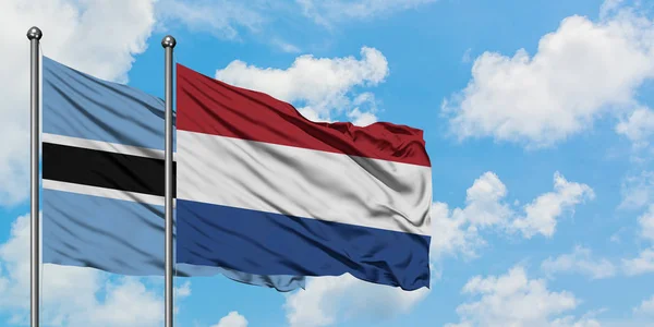 Bandera de Botswana y Holanda ondeando en el viento contra el cielo azul nublado blanco juntos. Concepto diplomático, relaciones internacionales . — Foto de Stock